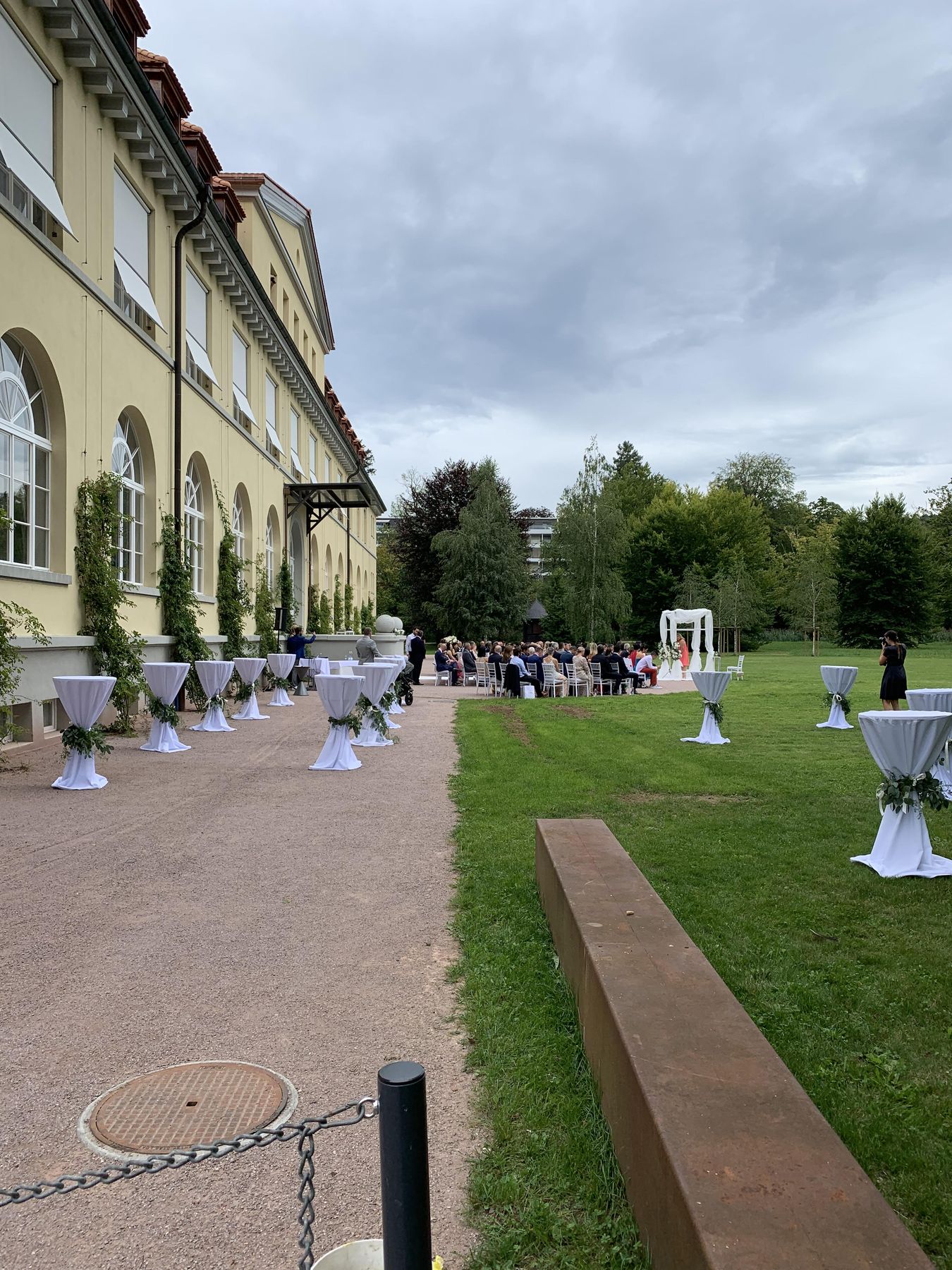 Destination wedding ceremony setup at a European castle – outdoor cocktail tables, guests, classical venue facade