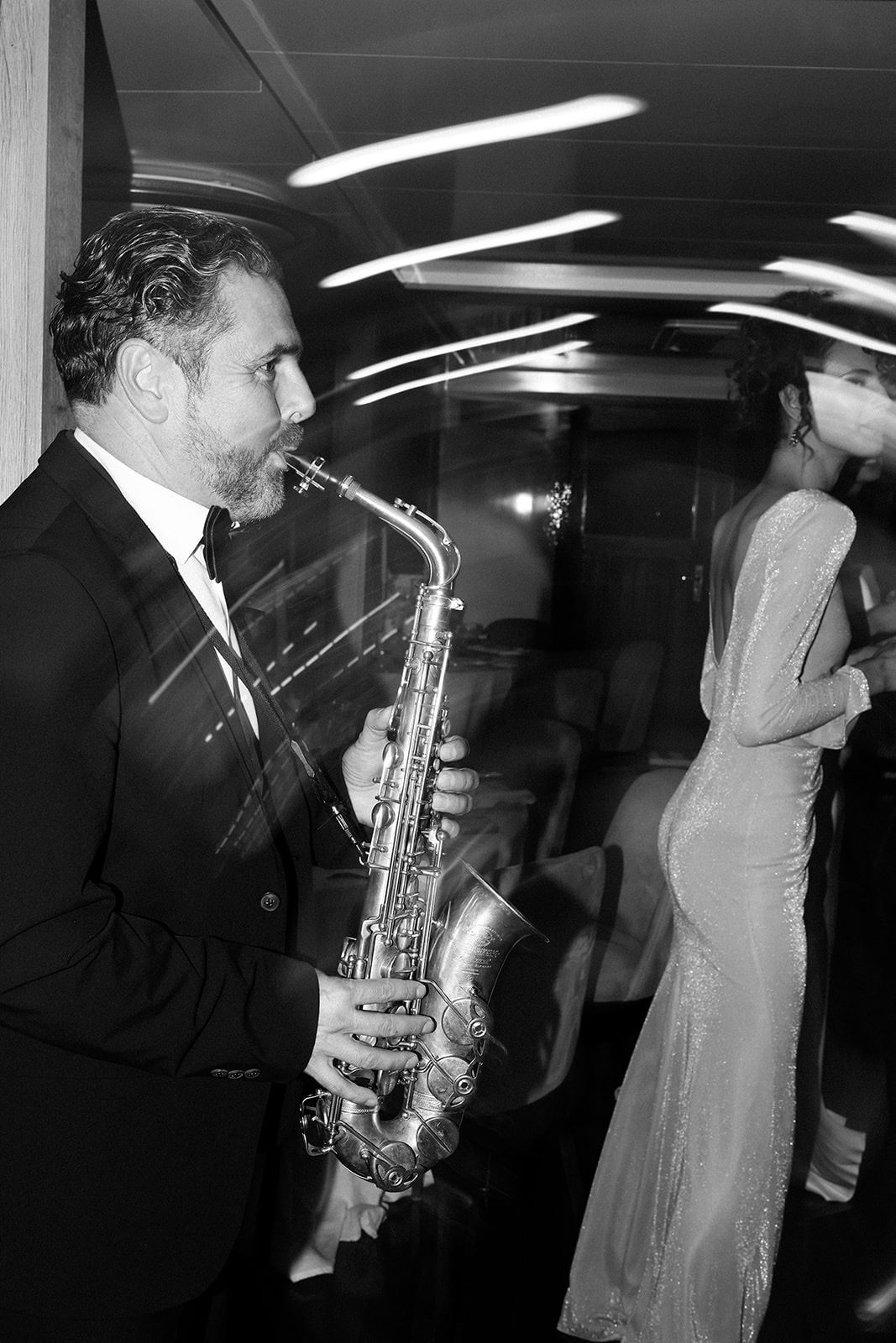 Večernji sax set u salonu jahte – saksofonist u tuxedu, žena u svjetlucavoj haljini, motion blur, crno-bijela editorial fotografija